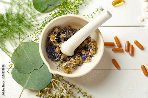 Mortar with dry flowers, herbs and plant based pills on table photo