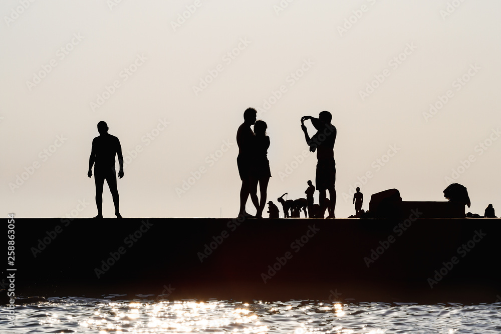 Silhouettes of people being photographed on the sea pier. Rest on the sea beach. Couple in love
