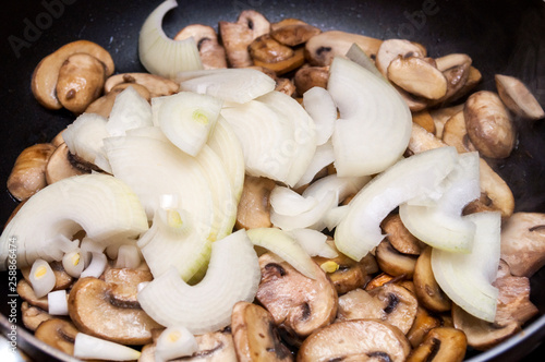 Fresh champignons and onions are fried in a pan.