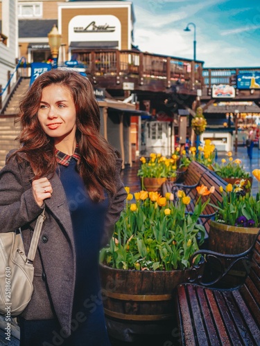 Girl with long hair in a coat walking on the pier in San Francisco on the background of yellow tulips