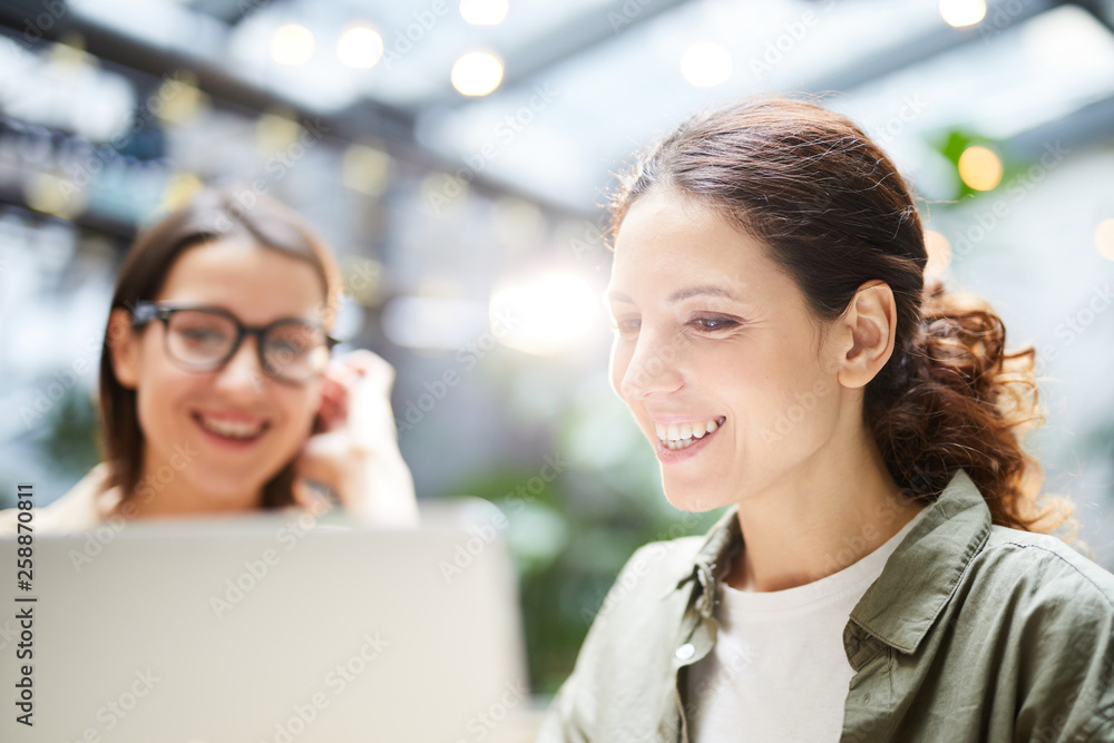 Obraz premium Close-up of cheerful lady programmers using laptop while creating landing page together, they working in cafe