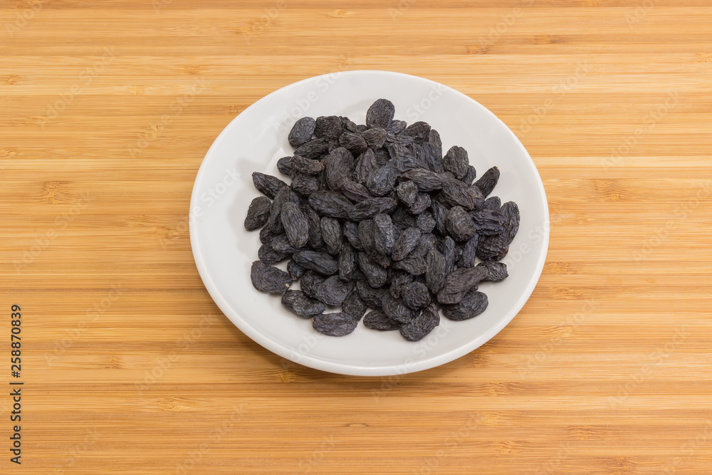 Raisins on the saucer on a wooden surface Raisins on the saucer on a wooden surface