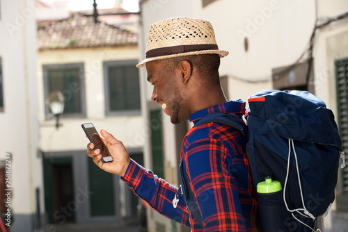 side portrait of happy african american man with backpack and mobile phone