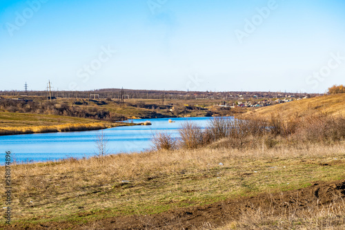 Fototapeta Naklejka Na Ścianę i Meble -  Early spring landscape, in the Rostov region in the city of Shakhty, on the Grushevka river. Sunny sunset in yellow and orange warm light. Dry grass on the local shore and a beautiful reflection in th