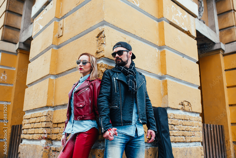 Cool couple in leather jackets standing embraced holding electric guitar