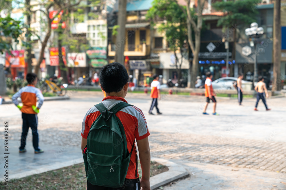 Lonely Asian school boy watches his friends play football outdoor in city Lonely Asian school boy watches his friends play football outdoor in city