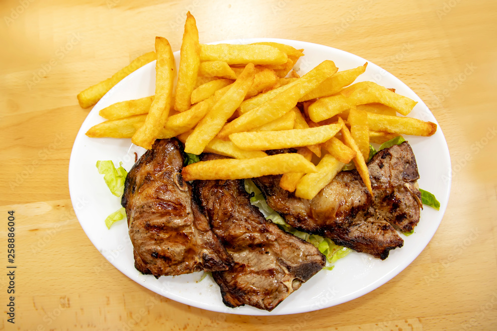 Grilled lamb ribs with french fries on a plate on a wooden table Grilled lamb ribs with french fries on a plate on a wooden table