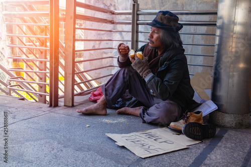 Homeless man is sitting down on walkway in town. He Eating bread.He is very glad and happy. poverty, despair, Photo Sympathetic and hope concept.