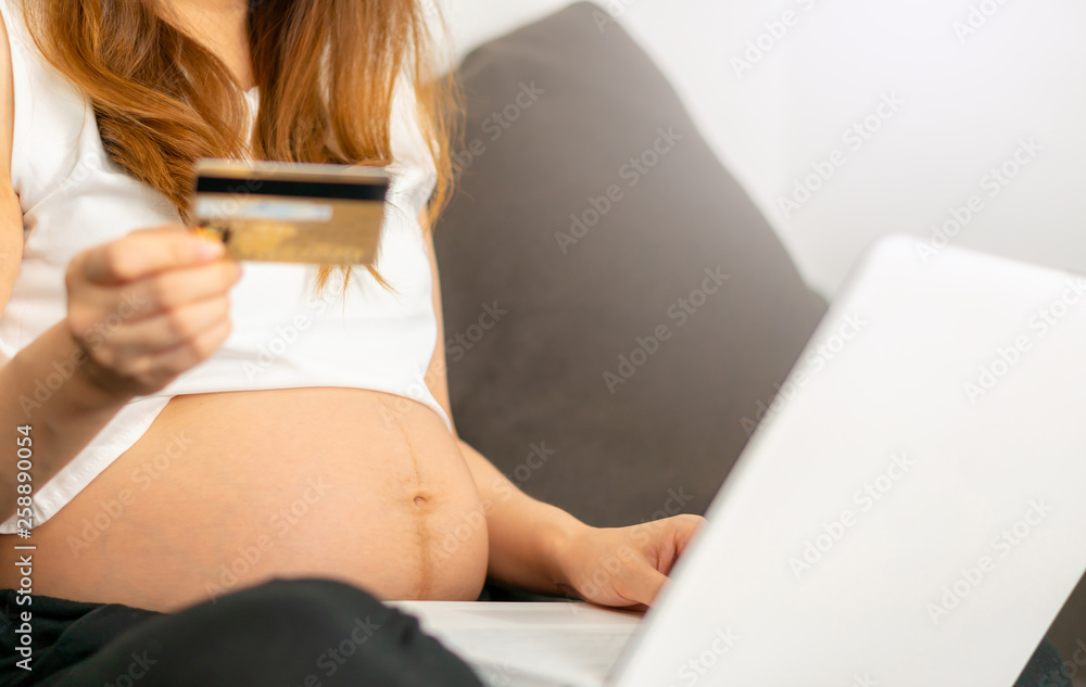 Naklejka premium Happy young pregnant online shopping with smartphone and credit card at home