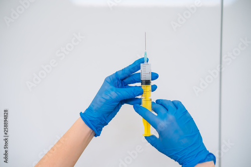 Hands in rubber gloves hold a disposable medical syringe with the drug