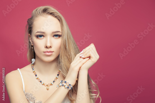 Perfect blonde woman with golden chain earrings, bracelet and necklace. Jewelry girl on pink background photo