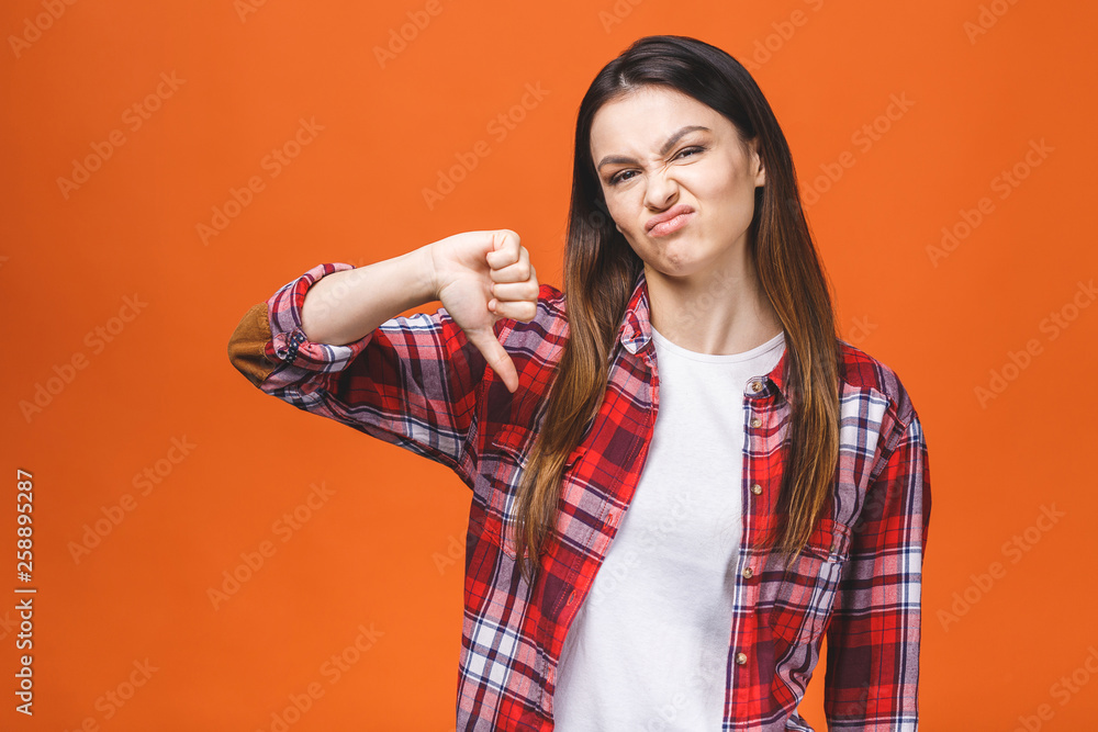 Portrait of a young woman showing thumbs down gesture over orange background. Portrait of a young woman showing thumbs down gesture over orange background.
