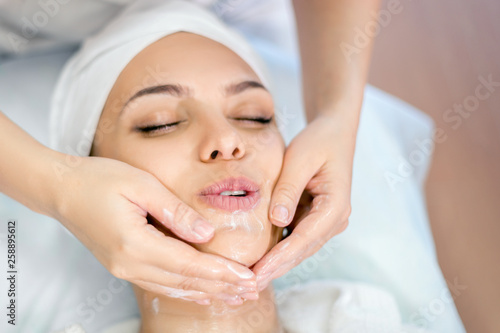 Cosmetology. The hands of a cosmetologist do a facial massage with a mask. Young beautiful girl on spa procedure.