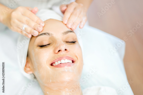 Cosmetology. Close up of cosmetologist hands doing face massage with mask. Smiling beautiful girl on spa procedure.