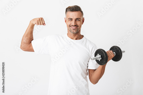 Image of bodybuilder man 30s with bristle wearing casual t-shirt pumping biceps and lifting dumbbell