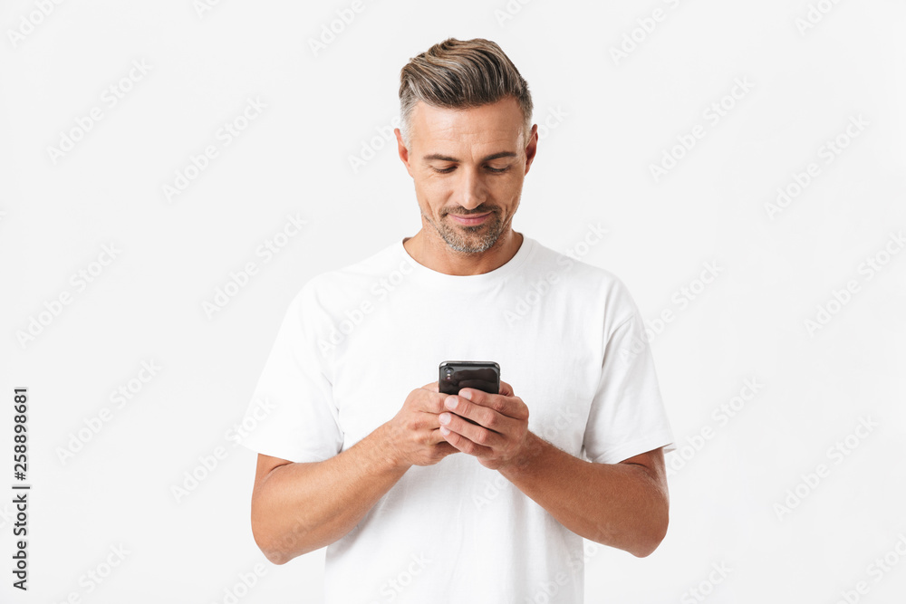 Image of brunette man 30s wearing casual t-shirt holding and using smartphone Image of brunette man 30s wearing casual t-shirt holding and using smartphone