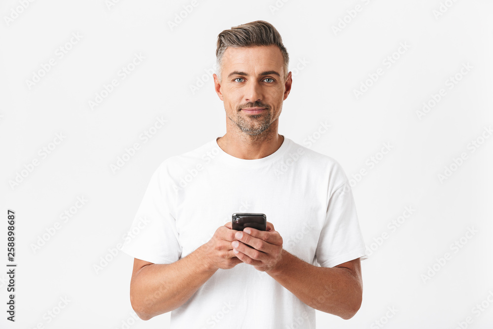 Image of muscular man 30s wearing casual t-shirt holding and using smartphone Image of muscular man 30s wearing casual t-shirt holding and using smartphone