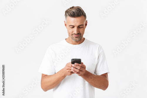 Image of brunette man 30s wearing casual t-shirt holding and using smartphone © Drobot Dean