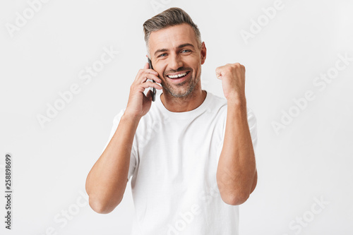 Image of happy man 30s wearing casual t-shirt holding smartphone and having mobile conversation