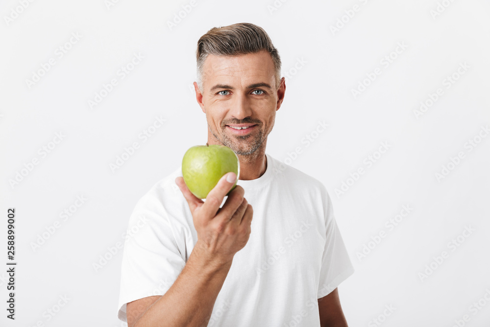 Image of happy man 30s with bristle posing on camera and holding green apple in hand Image of happy man 30s with bristle posing on camera and holding green apple in hand