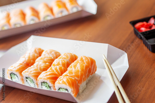 Philadelphia rolls classic on the wooden table. Salmon, cheese, cucumber, avocado, wooden sticks. Japanese sushi home delivery. Top view, flat lay