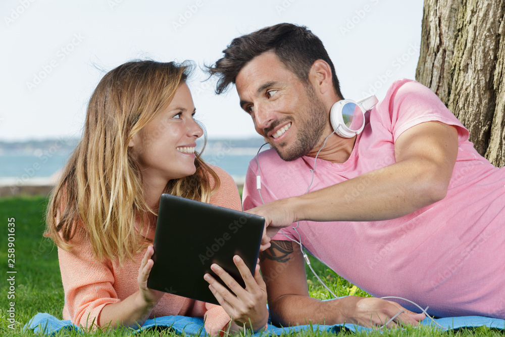 couple laying on grass checking the tablet couple laying on grass checking the tablet