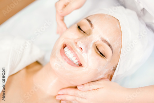 Beautician makes facial massage with mask. Beautiful smiling girl on spa procedure.
