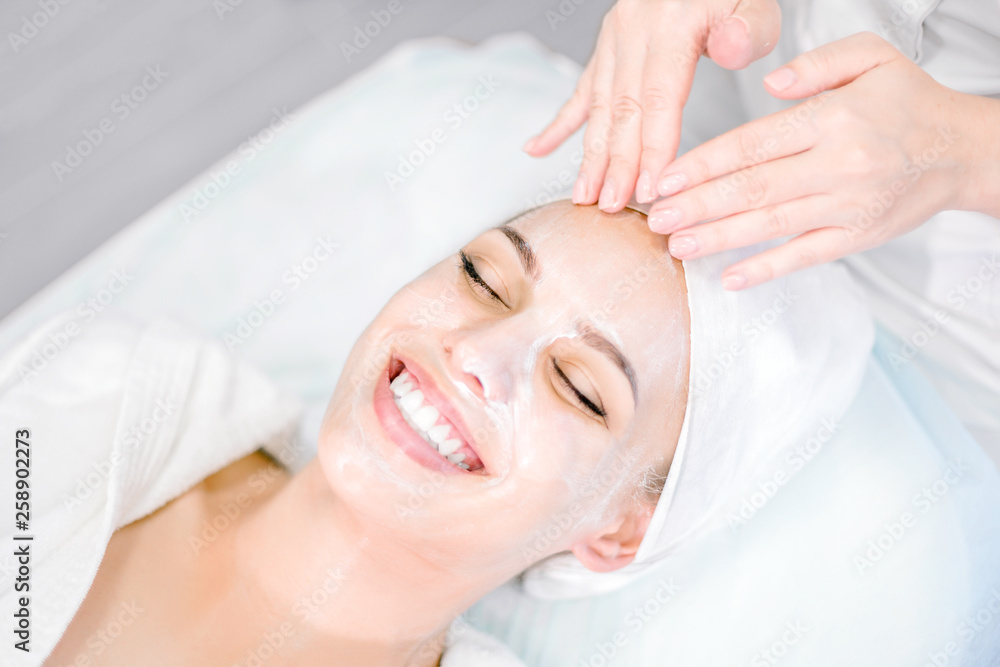 Beautician makes facial massage with mask. Beautiful smiling girl on spa procedure. Facial care.