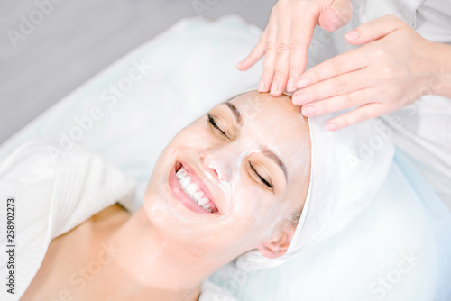 Beautician makes facial massage with mask. Beautiful smiling girl on spa procedure. Facial care. photo