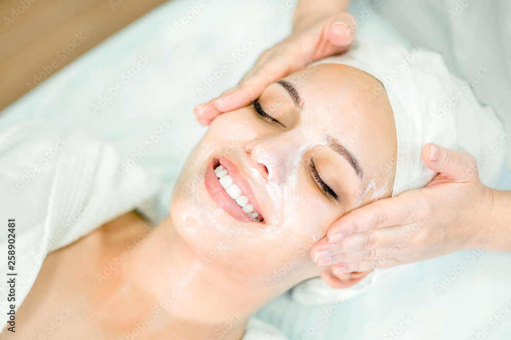 Beautician makes facial massage with mask. Beautiful smiling girl on spa procedure by face.