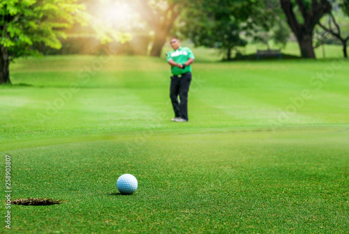 Golfer putting golf ball on the green golf with sun in morning time.