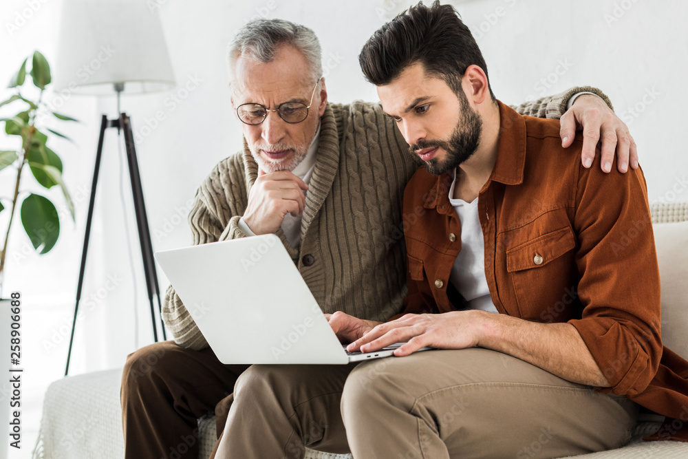 handsome man sitting with senior father and looking at laptop handsome man sitting with senior father and looking at laptop