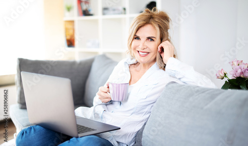 Sympathisch lächelnde Frau zuhause auf der Couch mit Laptop und Kaffee 