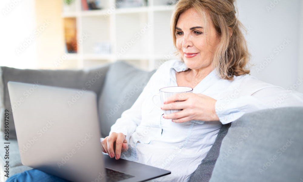 Sympathisch lächelnde Frau zuhause auf der Couch mit Laptop und Kaffee Sympathisch lächelnde Frau zuhause auf der Couch mit Laptop und Kaffee