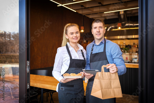Small business owners couple standing in doorway of trendy small restaurant serving food from online orders and attending customers 