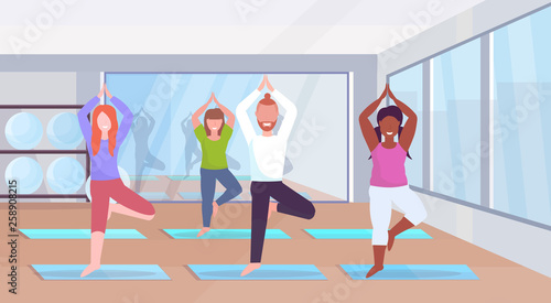 sporty man women group doing yoga exercises mix race people meditating standing in tree position working out healthy lifestyle concept modern gym studio interior full length