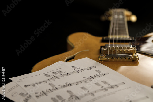 Vintage archtop guitar in natural maple close-up high angle view with music sheets on black background