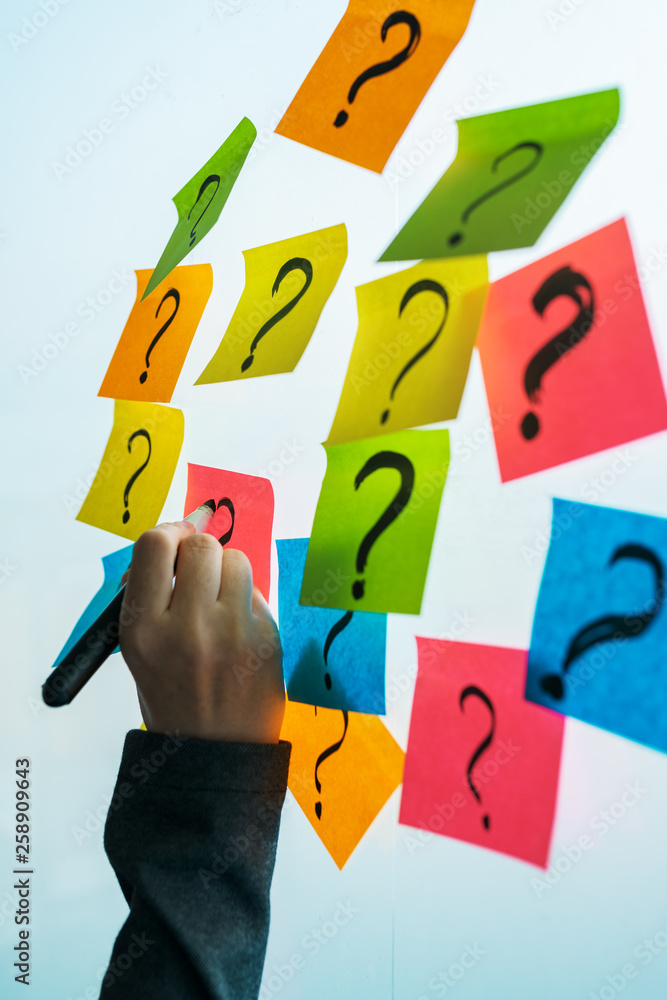 Businesswoman writing question marks on colorful sticky note paper Businesswoman writing question marks on colorful sticky note paper