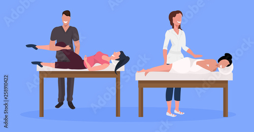 young female clients enjoying traditional massage man woman masseurs in coat massaging patients lying on bed luxury spa and wellness center concept horizontal full length blue background