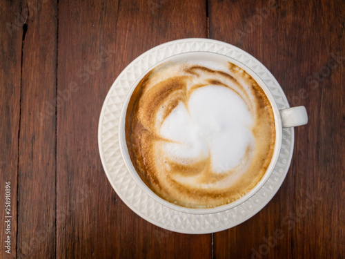 Smooth hot milk foam of cappuccino coffee on the beautiful vintage wooden table close up. Top angle image close up.