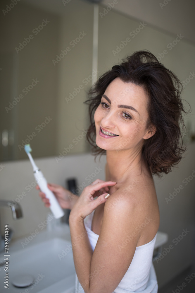 Pretty, middle aged woman brushing her teeth in a modern design bathroom Pretty, middle aged woman brushing her teeth in a modern design bathroom