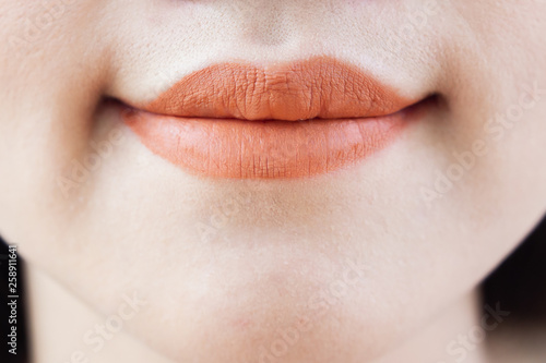 Asian woman's smilling mouth with pastel orange lipstick close up.