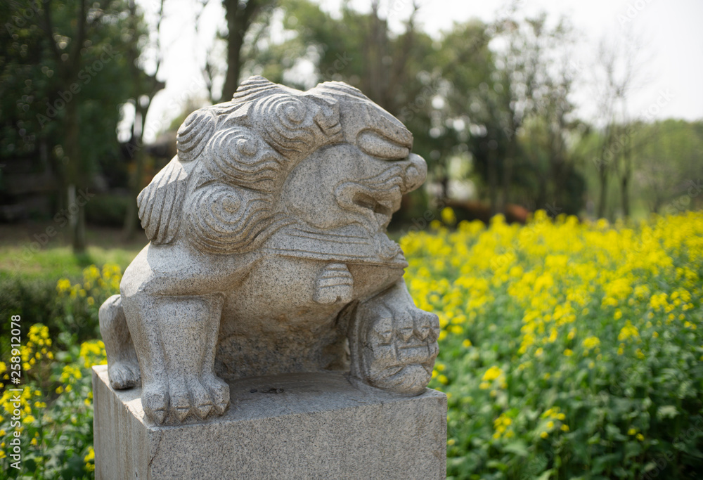 stone lion standing in rapeseed flowers field stone lion standing in rapeseed flowers field