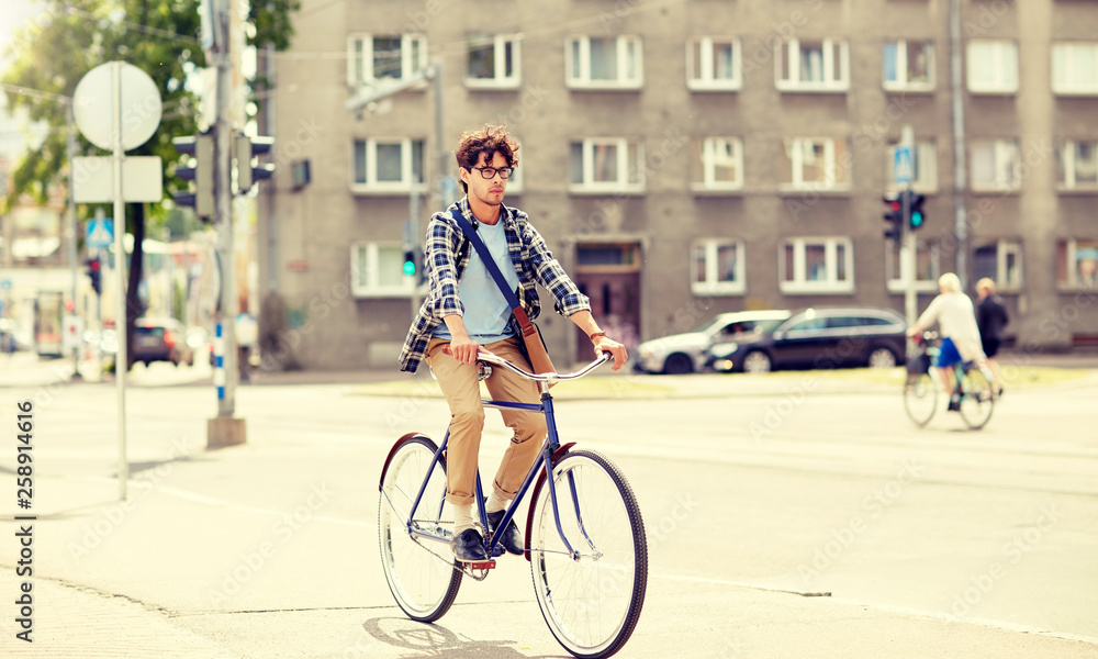 Fototapeta premium people, style, leisure and lifestyle - young hipster man with shoulder bag riding fixed gear bike on city street