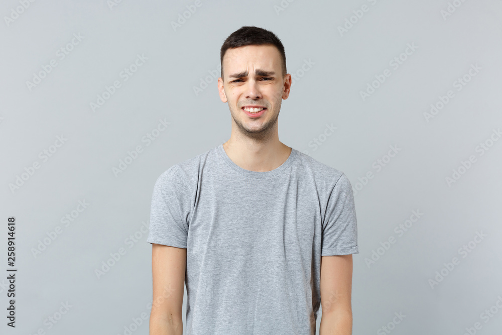 Portrait of crying upset dissatisfied young man in casual clothes standing, looking camera isolated on grey wall background in studio. People sincere emotions, lifestyle concept. Mock up copy space. Portrait of crying upset dissatisfied young man in casual clothes standing, looking camera isolated on grey wall background in studio. People sincere emotions, lifestyle concept. Mock up copy space.