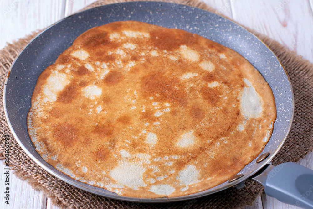 Frying pan with tasty thin pancakes on table
