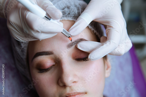 Permanent Makeup For Eyebrows. Microblading brow. Beautician Doing Eyebrow Tattooing For Female Face. Beautiful young girl in a beauty salon photo