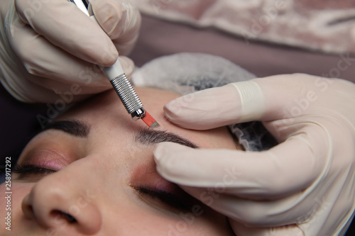 Permanent Makeup For Eyebrows. Microblading brow. Beautician Doing Eyebrow Tattooing For Female Face. Beautiful young girl in a beauty salon photo