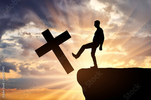 Man atheist pushes the symbol of christian cross into the cliff photo