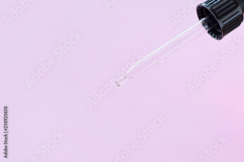Glass dropper with selective focus on neutral pink background. Glass pipette with drop of anti age serum. Transparent dropper with liquid essential. Pharmacy concept with empty space for text  © Tetiana Ivanova